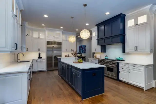 White kitchen with a navy island, a navy range hood, globe pendants and wood floors
