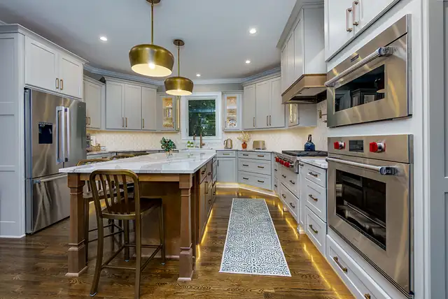 Kitchen with gray shaker cabinets, a stained wood island with marble top, brass dome pendants and a professional range