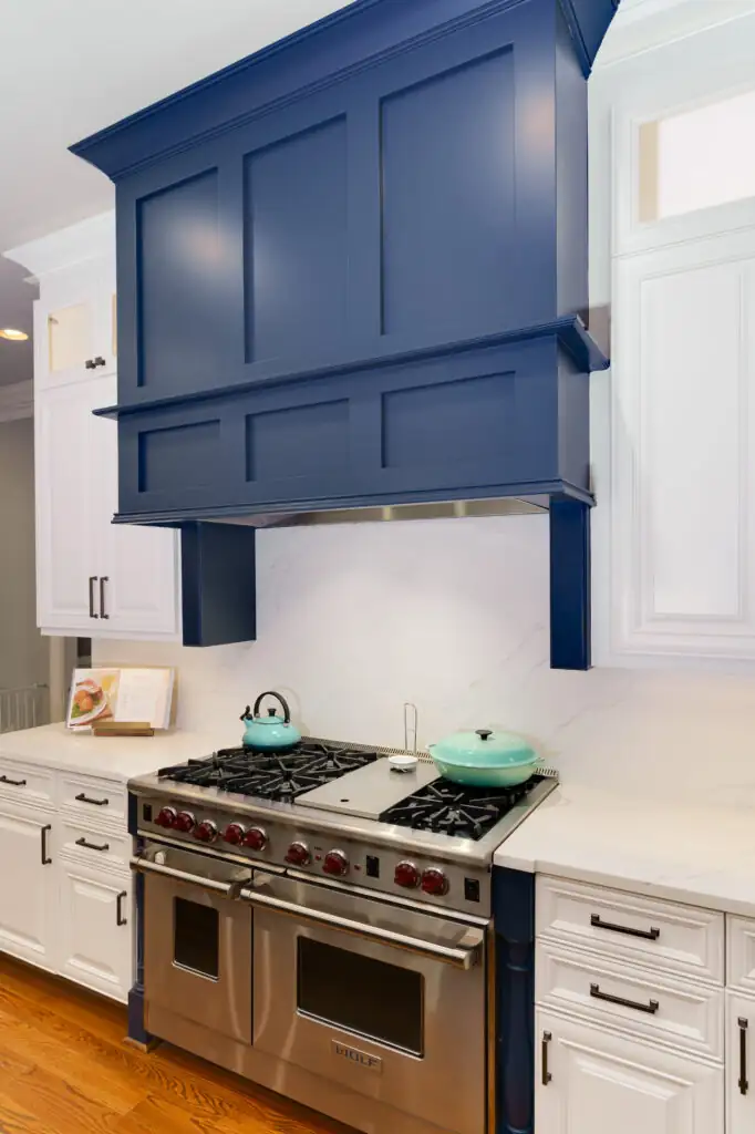 Navy blue range hood and custom cabinetry refinished above a professional range, with white cabinets on each side