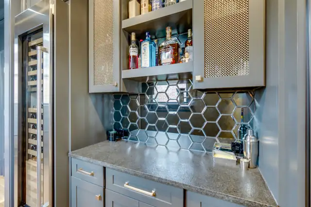 Home bar with painted gray cabinets, a mirrored hexagon tile backsplash, open liquor shelves and a wine fridge