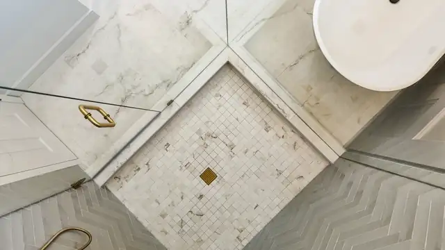 Bathroom vanity in deep navy with brass faucets, a white stone top and an arched black mirror between brass sconces