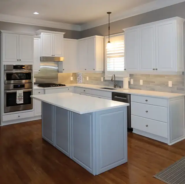 White kitchen with a blue-gray island, stone backsplash, stainless wall ovens and a pendant light over the sink