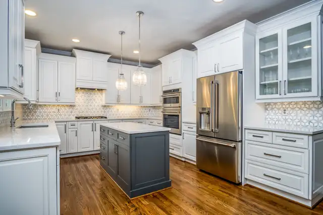 Two-tone kitchen with white cabinets, a navy island, glass pendants and a patterned tile backsplash