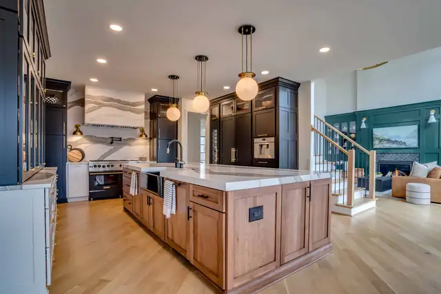 Remodeled kitchen with a stained wood island and white counter, glass globe pendants, navy cabinetry and an open stair to the living room